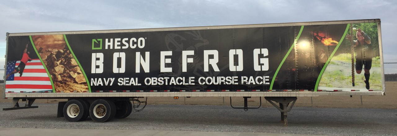 A trailer with “Hesco Bonefrog Navy SEAL Obstacle Course Race” and images of race participants running, an American flag graphic on the side, and bold car wraps highlighting the event’s branding.