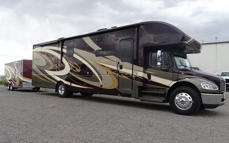 A brown and tan Accolade motorhome towing a matching enclosed trailer featuring custom bus wraps.