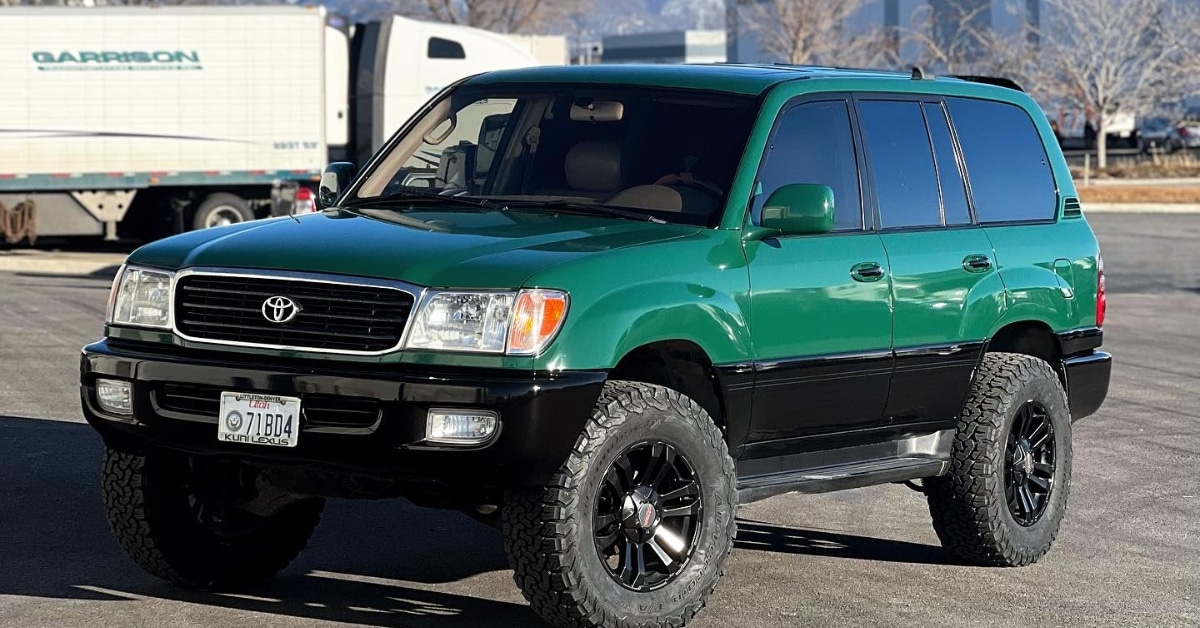A striking green and black SUV sits in the lot, showcasing off-road tires and a lift kit. Against a backdrop of trees and a truck, its sleek look might leave you wondering about the color change wrap cost that achieves such bold transformations.