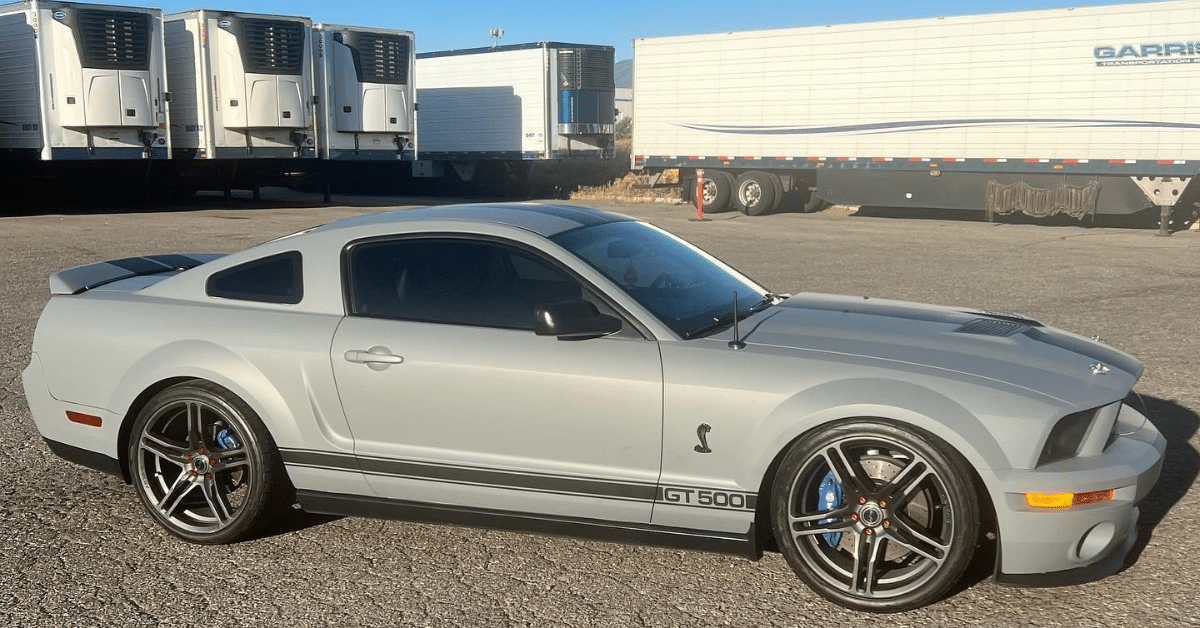 A sleek silver GT 500 sports car, with expertly applied car window tinting, gleams on the asphalt in front of several large trailers in Salt Lake City, UT.