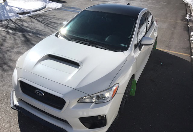 A white Subaru WRX with vinyl decals on its hood.
