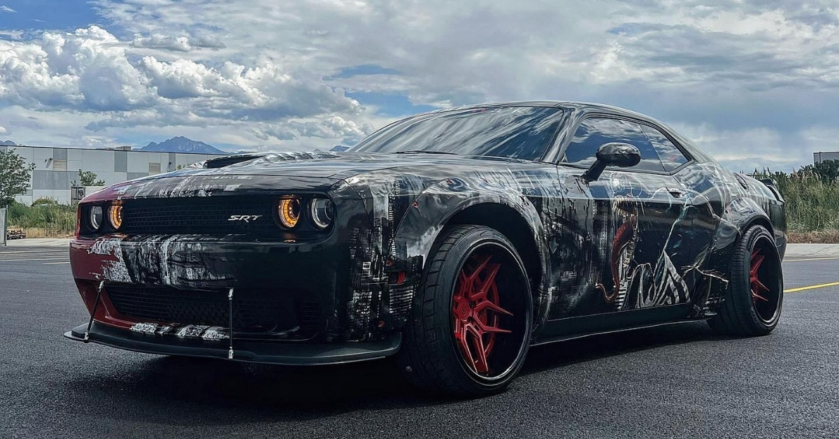 A black Dodge SRT with a vibrant vinyl car wrap featuring various designs and red wheels is parked on an asphalt surface, set against the cloudy sky of Salt Lake City, Utah.