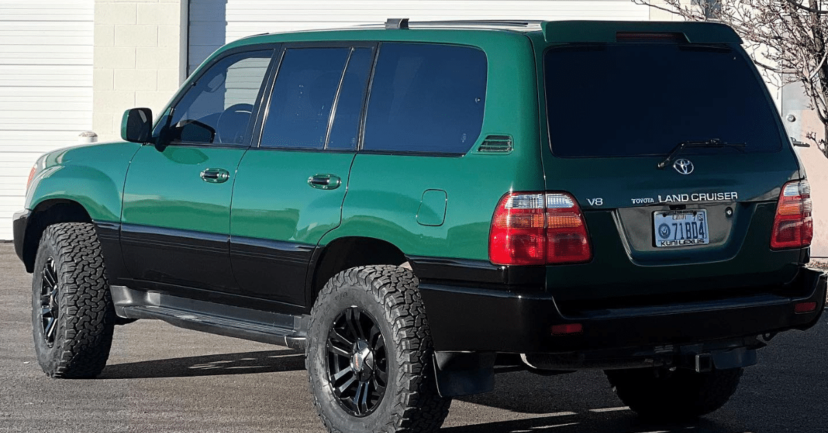 The green Toyota Land Cruiser SUV, sporting black trim and off-road tires, sits gleaming in the sun near a white garage door. Its sleek design is enhanced by expert car window tinting from Salt Lake City, offering both style and shade.