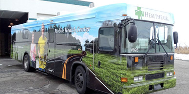 A bus with vinyl decals is parked in front of a garage.