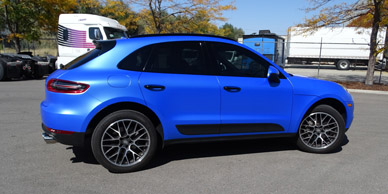 A blue Porsche Macan with vinyl decals is parked in a parking lot.