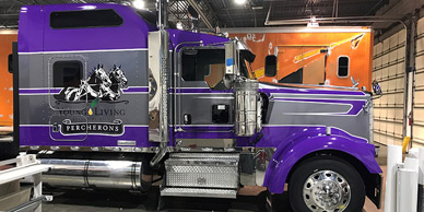 A purple and silver semi truck with vinyl decals is parked in a garage.