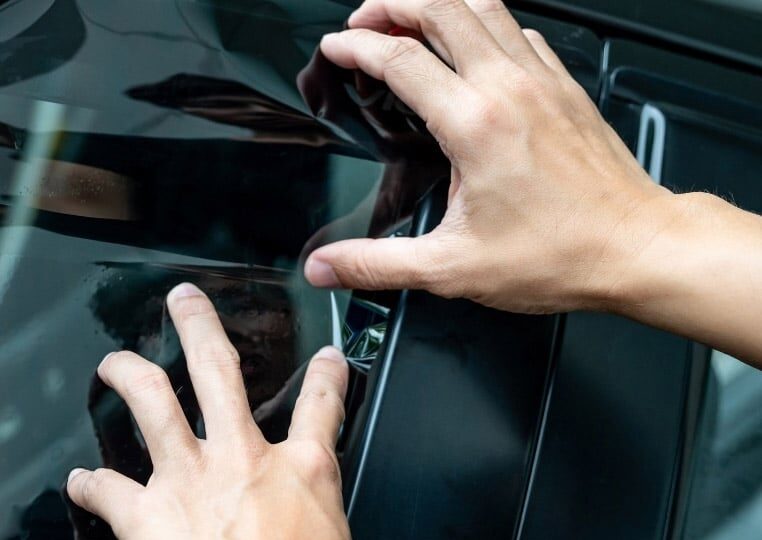Hands meticulously apply a sleek black window tint to a car window, showcasing expert car window tinting in Salt Lake City, Utah.